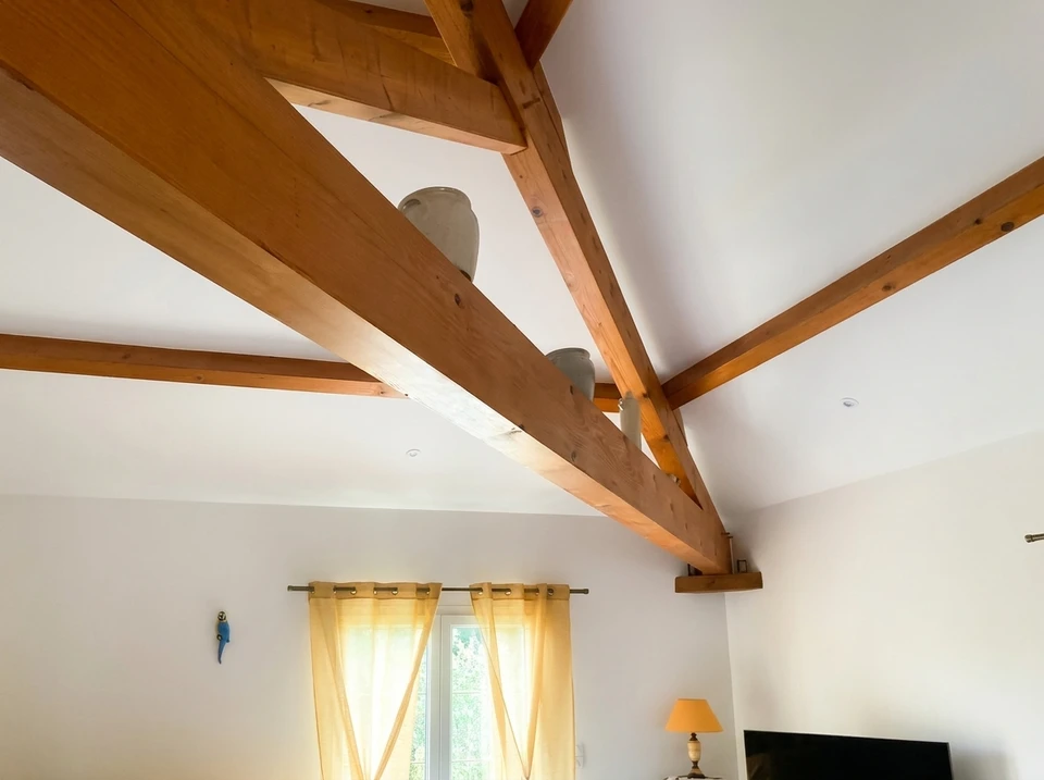 Photographe d'un ouvrier du bâtiment en tenue de travail appliquant de la peinture sur un mur intérieur avec un pinceau, montrant les différentes étapes de travail : à gauche du cadre, des plaques de plâtre partiellement installées, au centre l'ouvrier peignant méthodiquement, et à droite un mur déjà partiellement fini. La scène capture le professionnalisme et la progression du travail de rénovation intérieure, avec outils et matériaux visibles en arrière-plan.